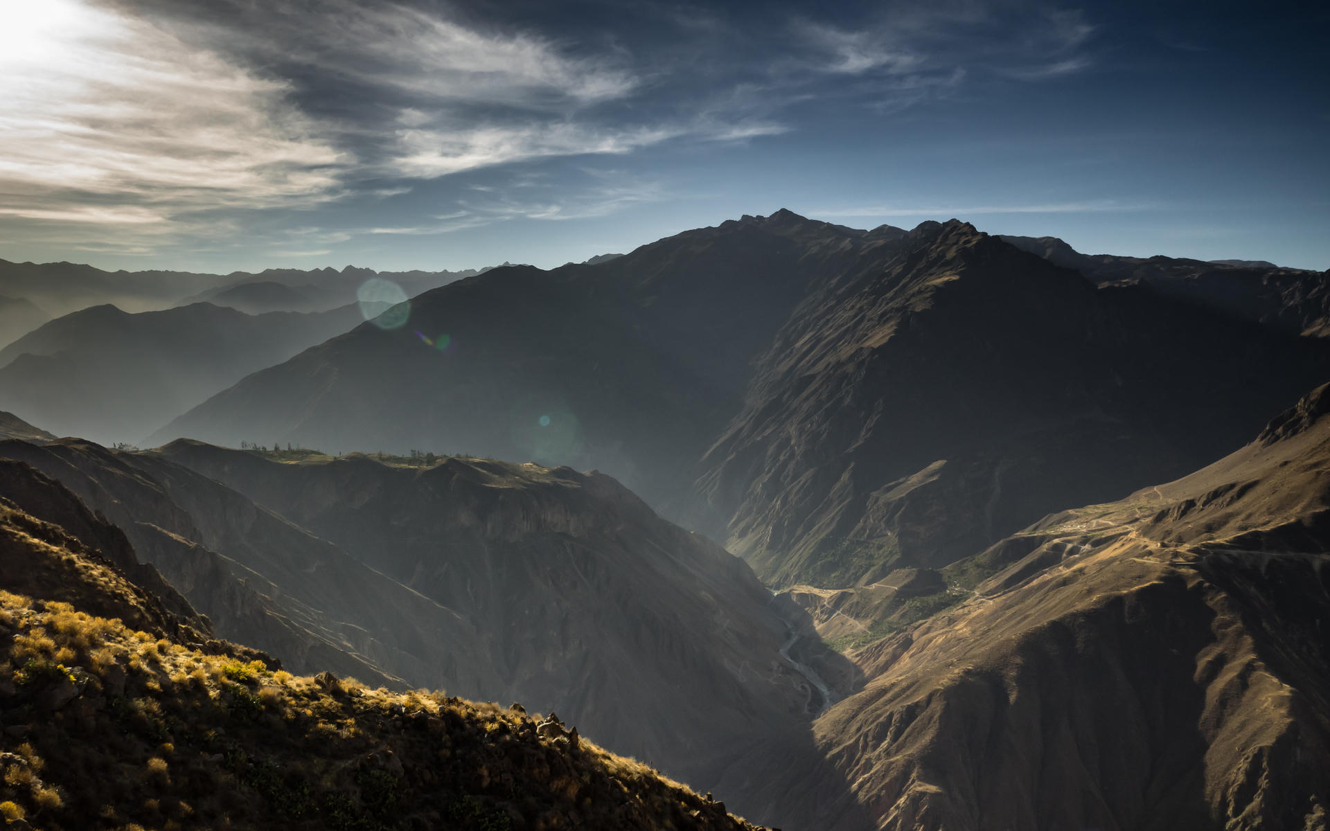 Mountains under cloudy sky with rays of sunlight breaking through, casting shadows on the slopes and valleys below.