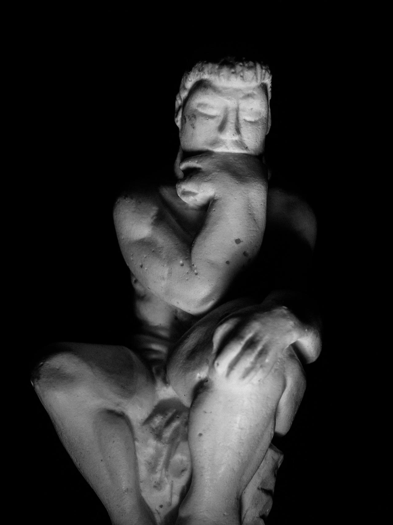 A figure crouching with eyes closed, illuminated against a dark background in monochrome.