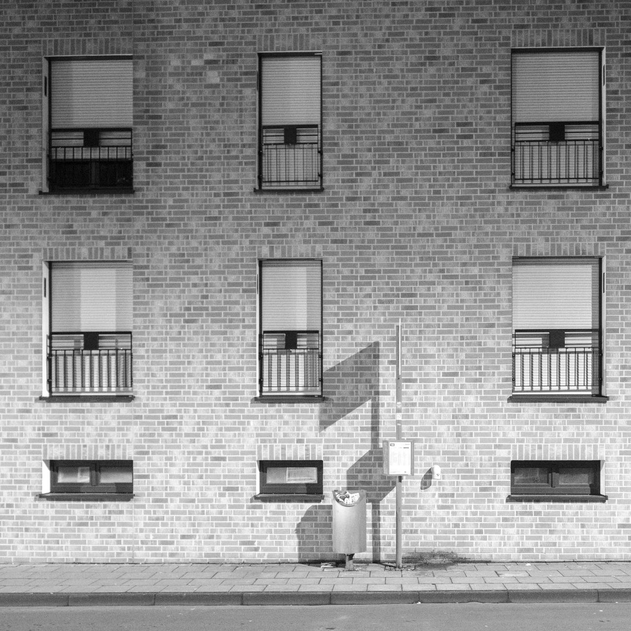 Brick building facade with six windows, three streetlights casting shadows on the wall.