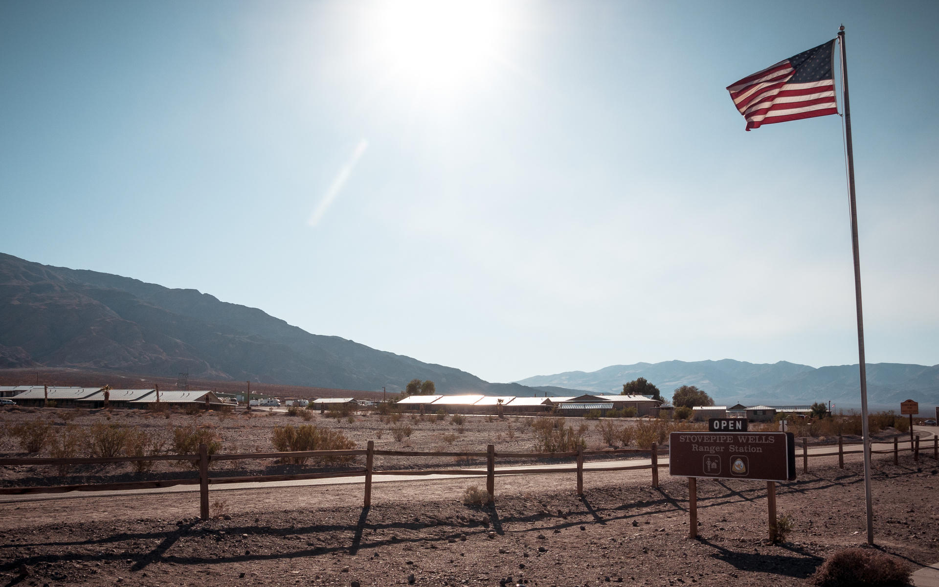 American flag waving in desert landscape, mountains in background, sign post below.