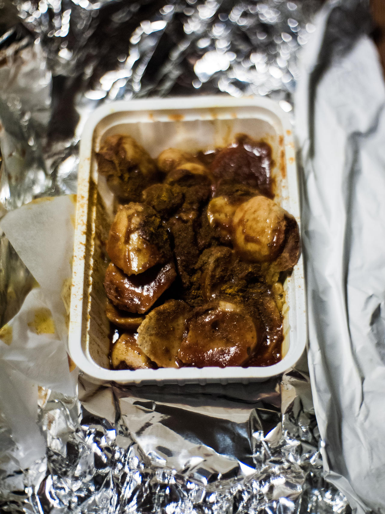 A takeout container with roasted meat, foil, and napkin underneath.