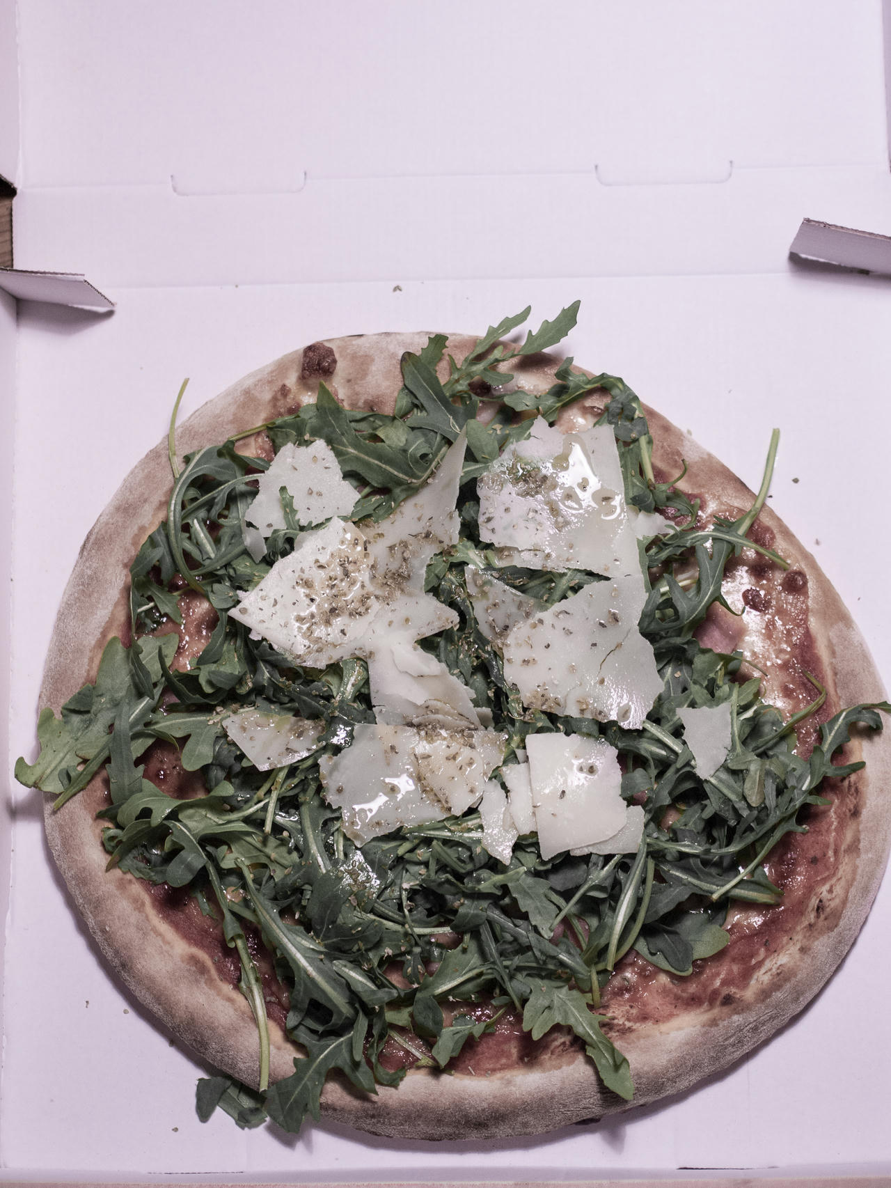 Pizza with arugula leaves and shaved cheese on a white box.