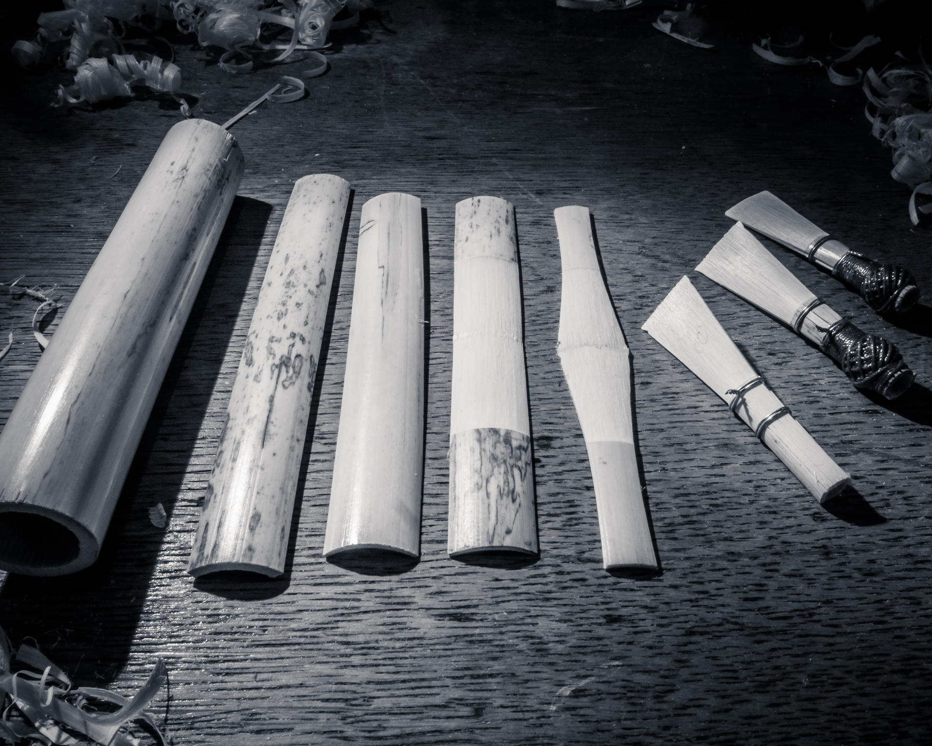 Five bamboo sticks in various stages of being hollowed out on a workbench, with tools nearby.