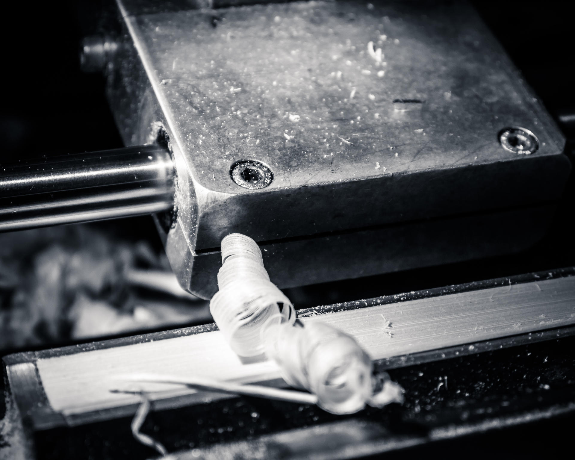 Hand in glove operating a machine with visible gears and bolts, black and white.