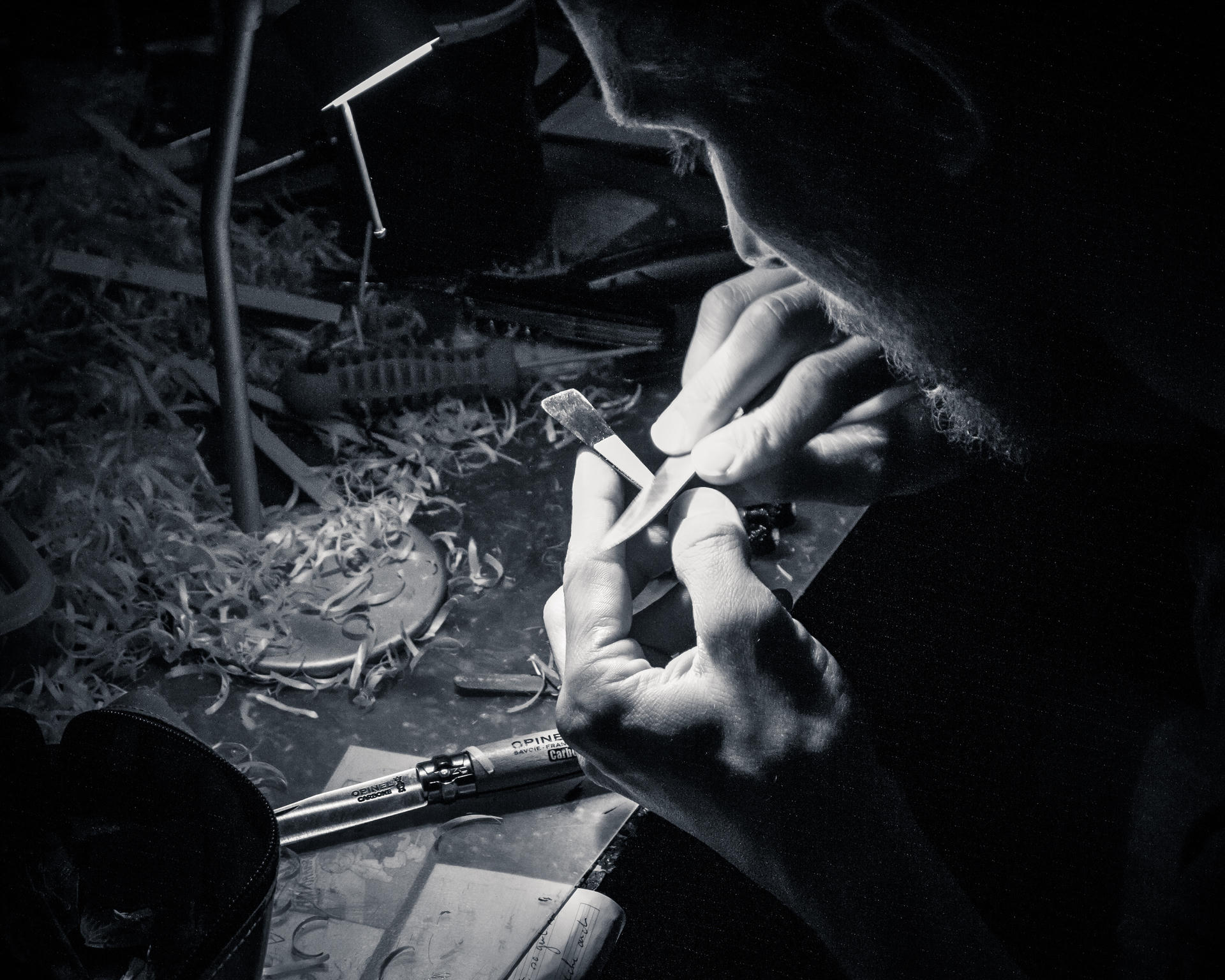 A pair of hands using a tool in a dimly lit workshop, with tools and debris on the floor.