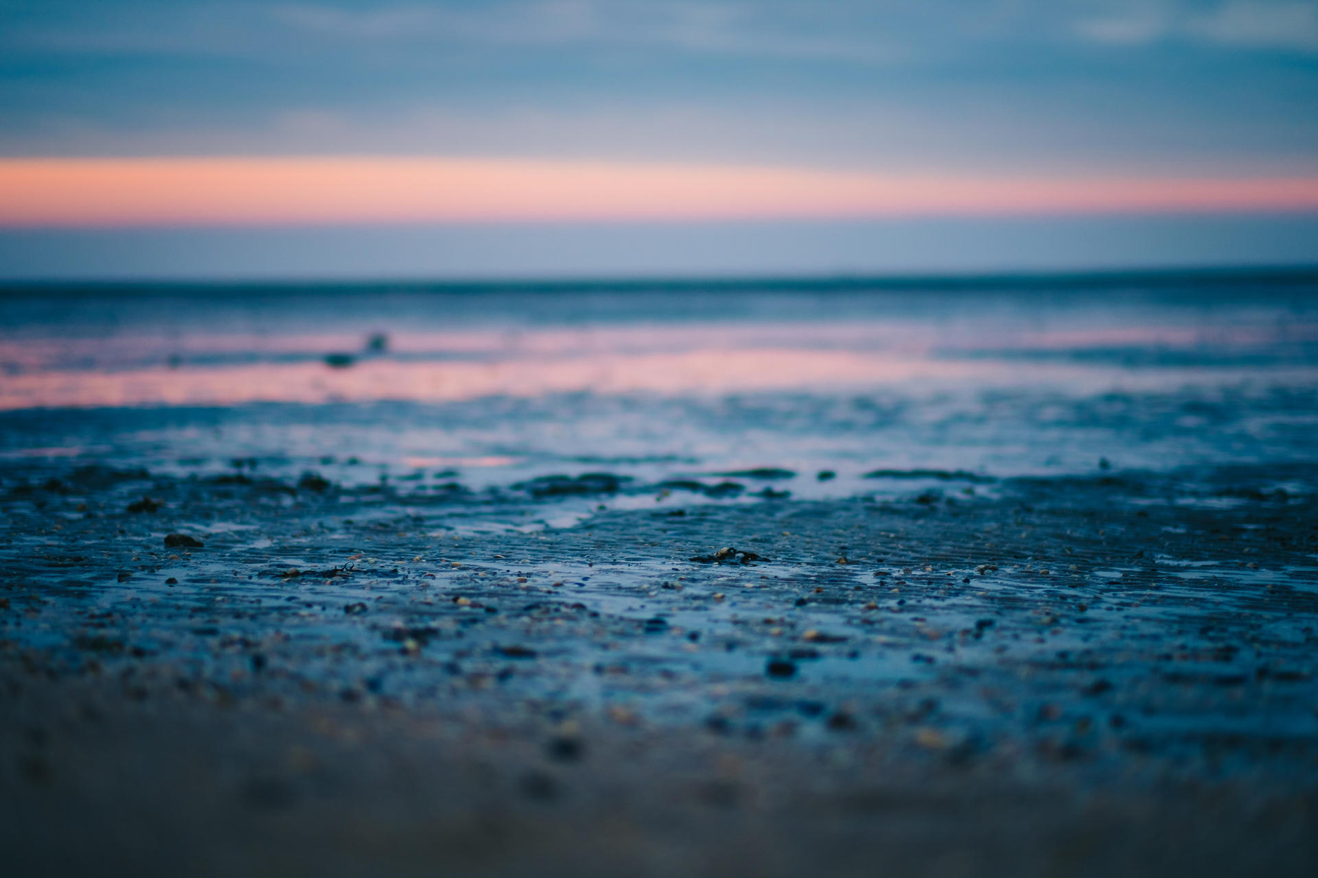 Beach at sunset with blurred horizon, pebbles in foreground.