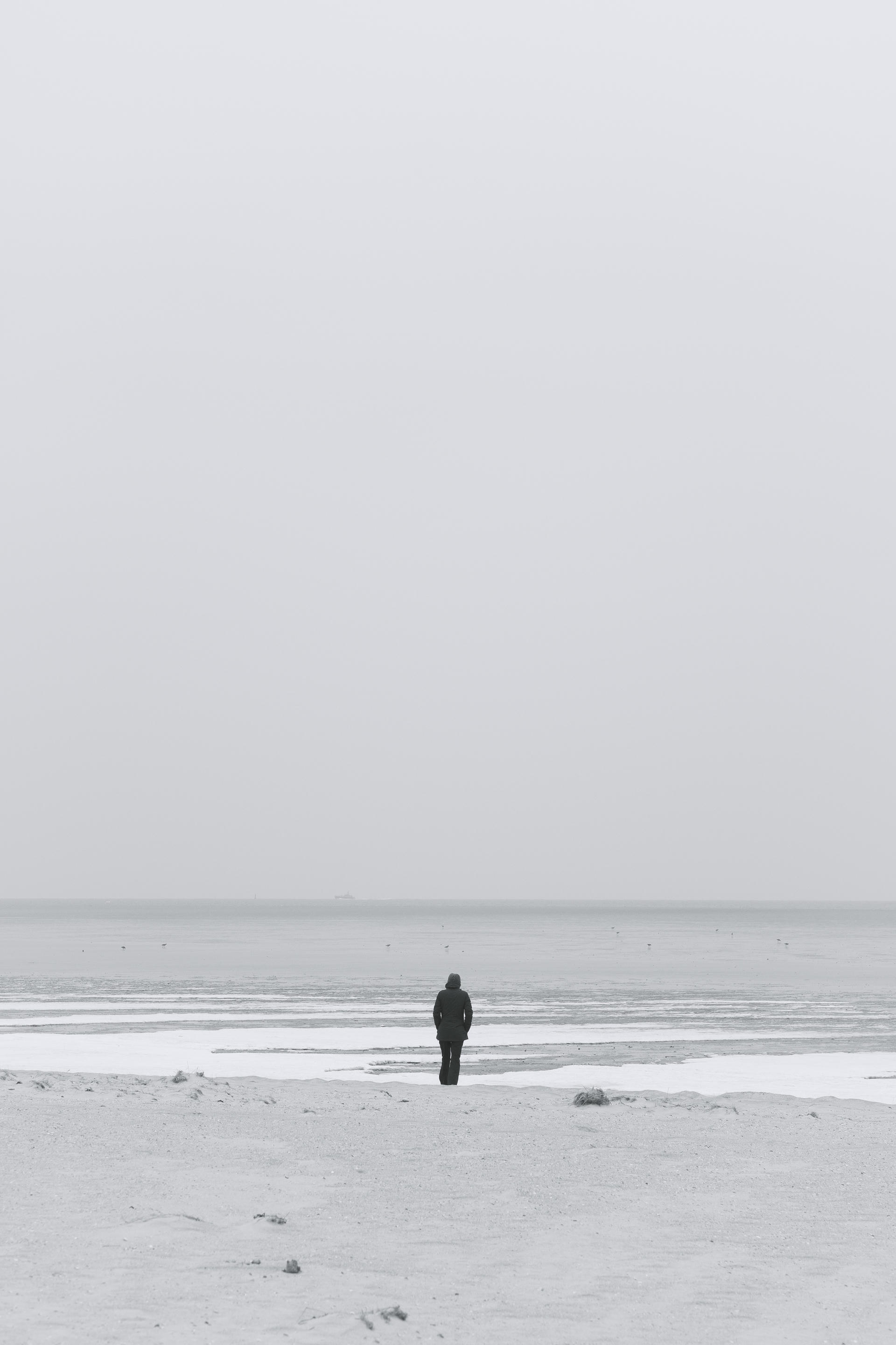 A solitary figure stands on a vast, empty beach with the ocean in the background.