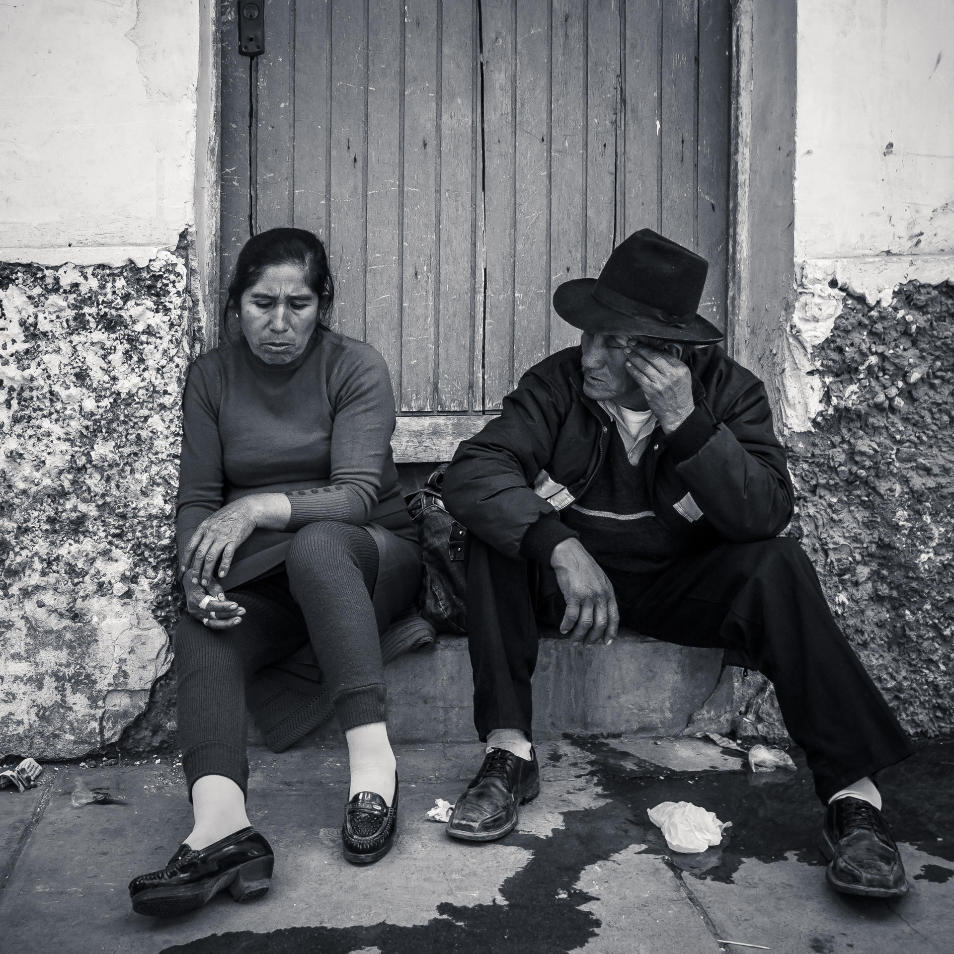 Two people sitting outside a wooden door, one resting her head on her hand, the other with his face covered.