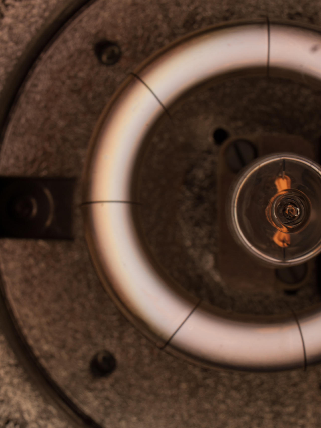 Close-up of an incandescent light bulb with a glowing filament, surrounded by concentric circles of light and shadow.