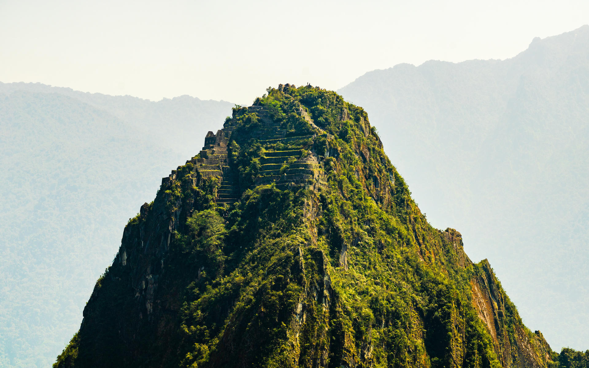 A green mountain with terraced steps, set against hazy mountains in the background.