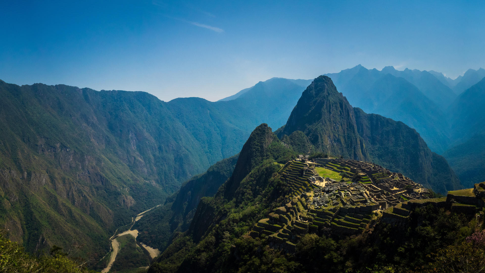 Mountainous landscape with ancient ruins in a valley, under a clear blue sky.