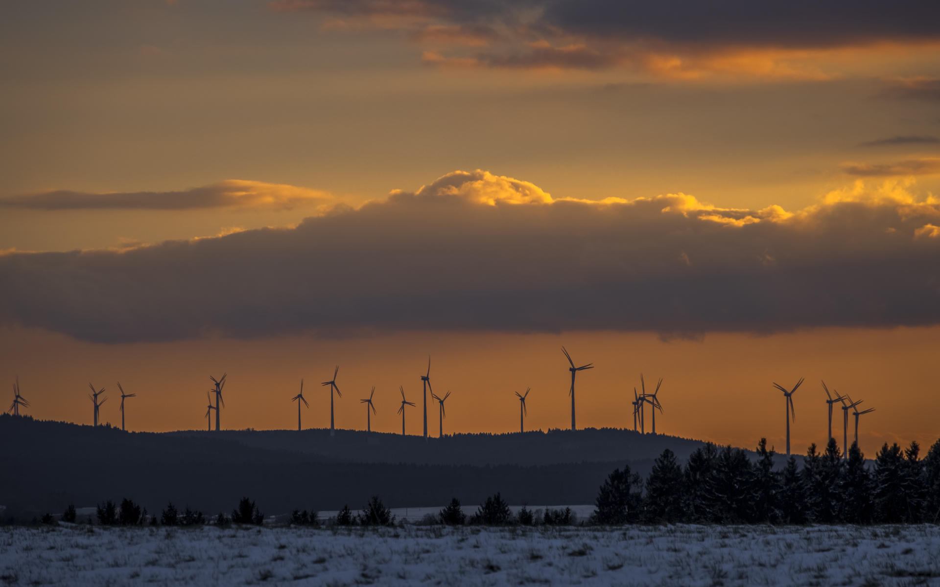 Sunset with wind turbines silhouetted against a colorful sky, snowy landscape.