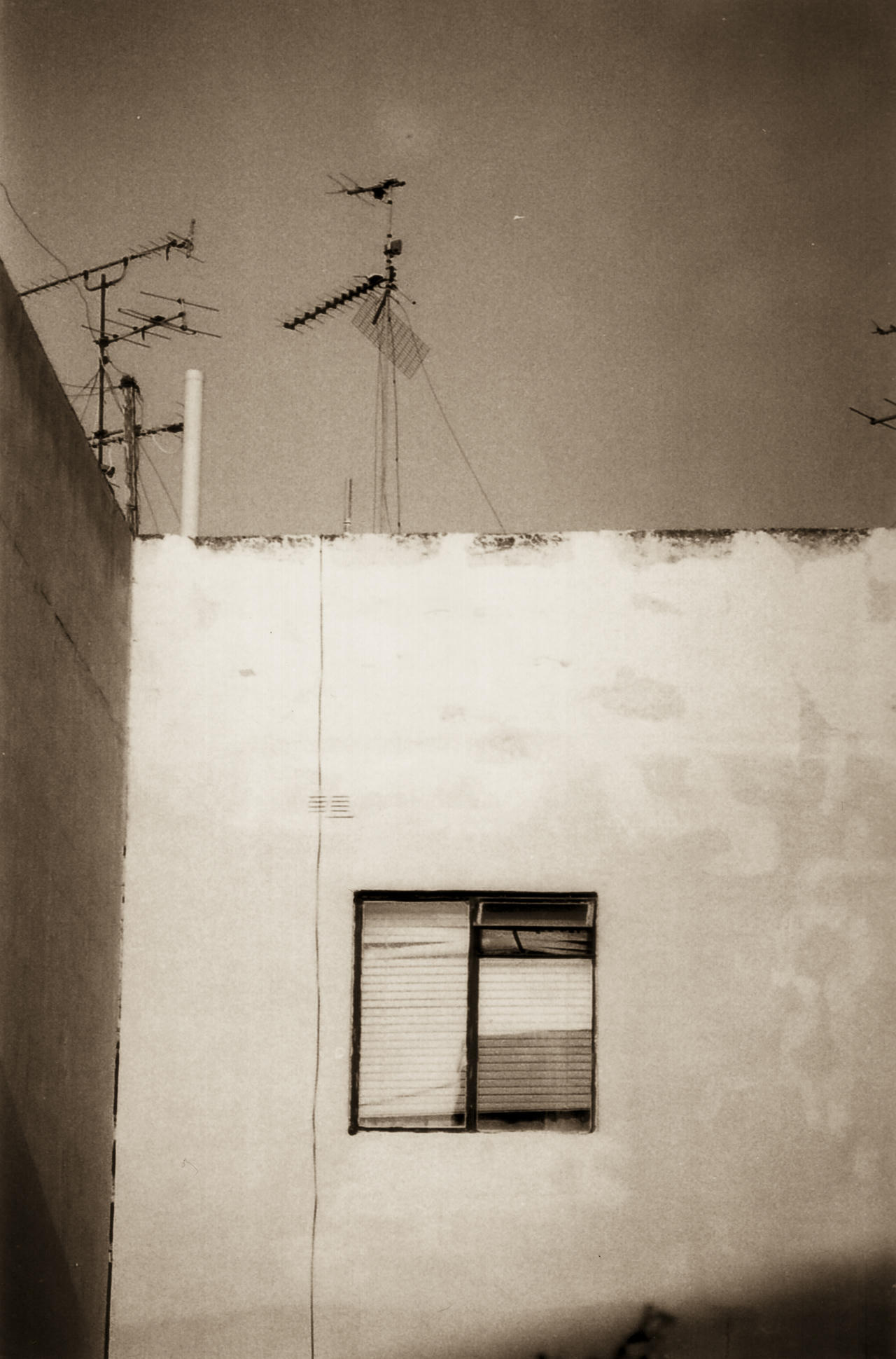 Building with two antennas on roof, single window below.