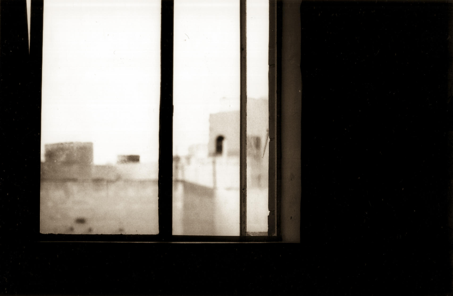 Window framed by white, showing buildings in background, soft focus, black and white photo.