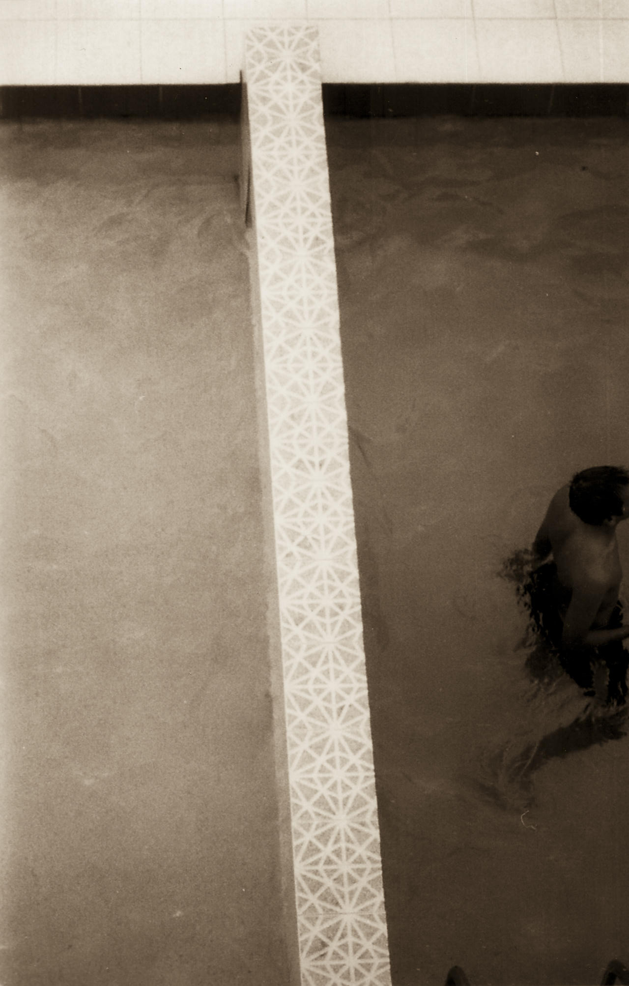 A person's reflection in a mirror next to a tiled wall.