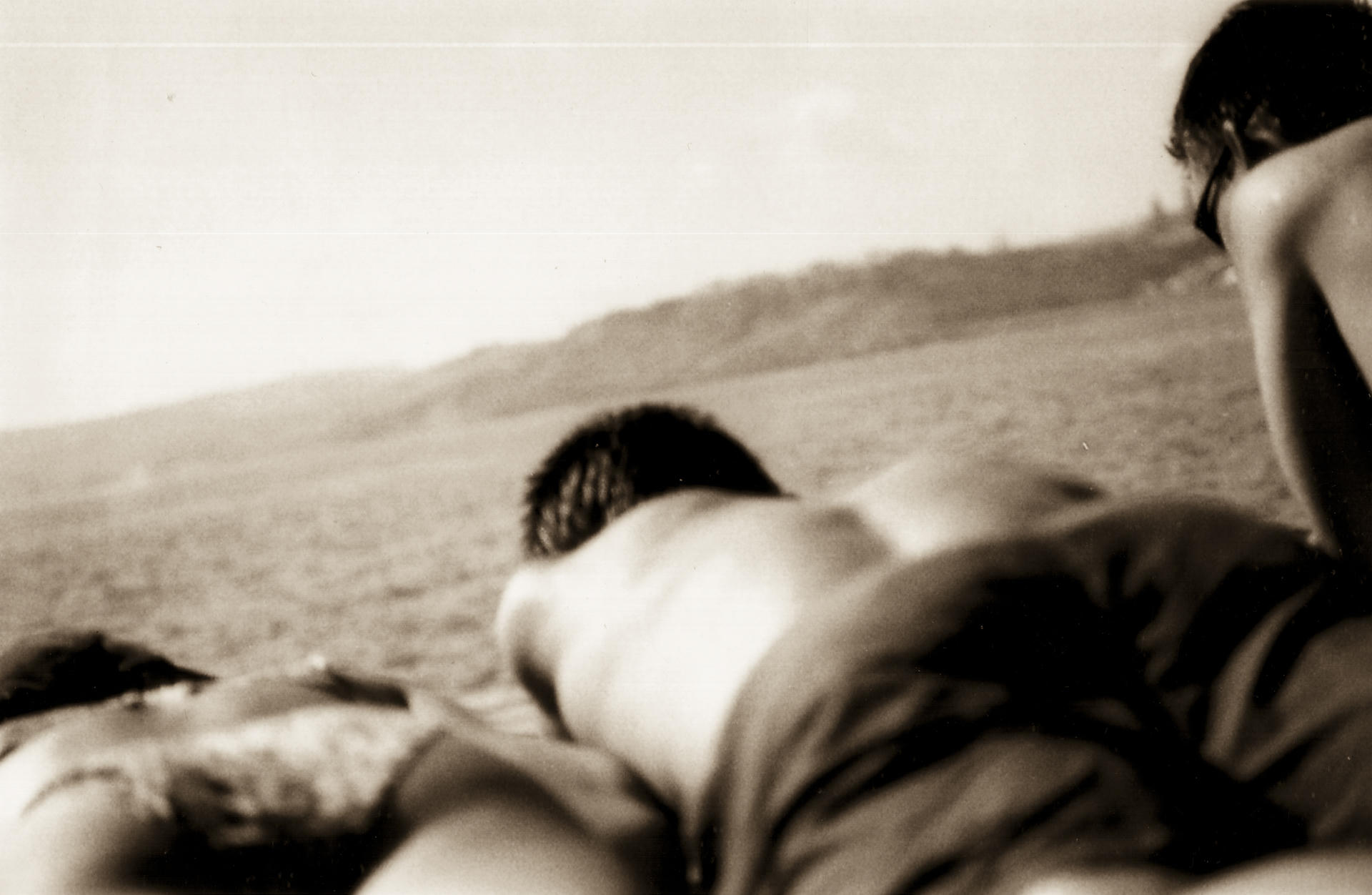 Couple lying on the ground, looking at a vast landscape with hills in the distance.