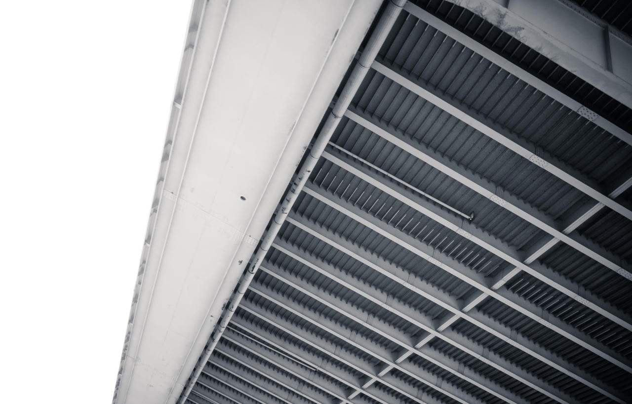 A close-up of a building's white exterior wall with vertical slats, viewed from below against a sky background.