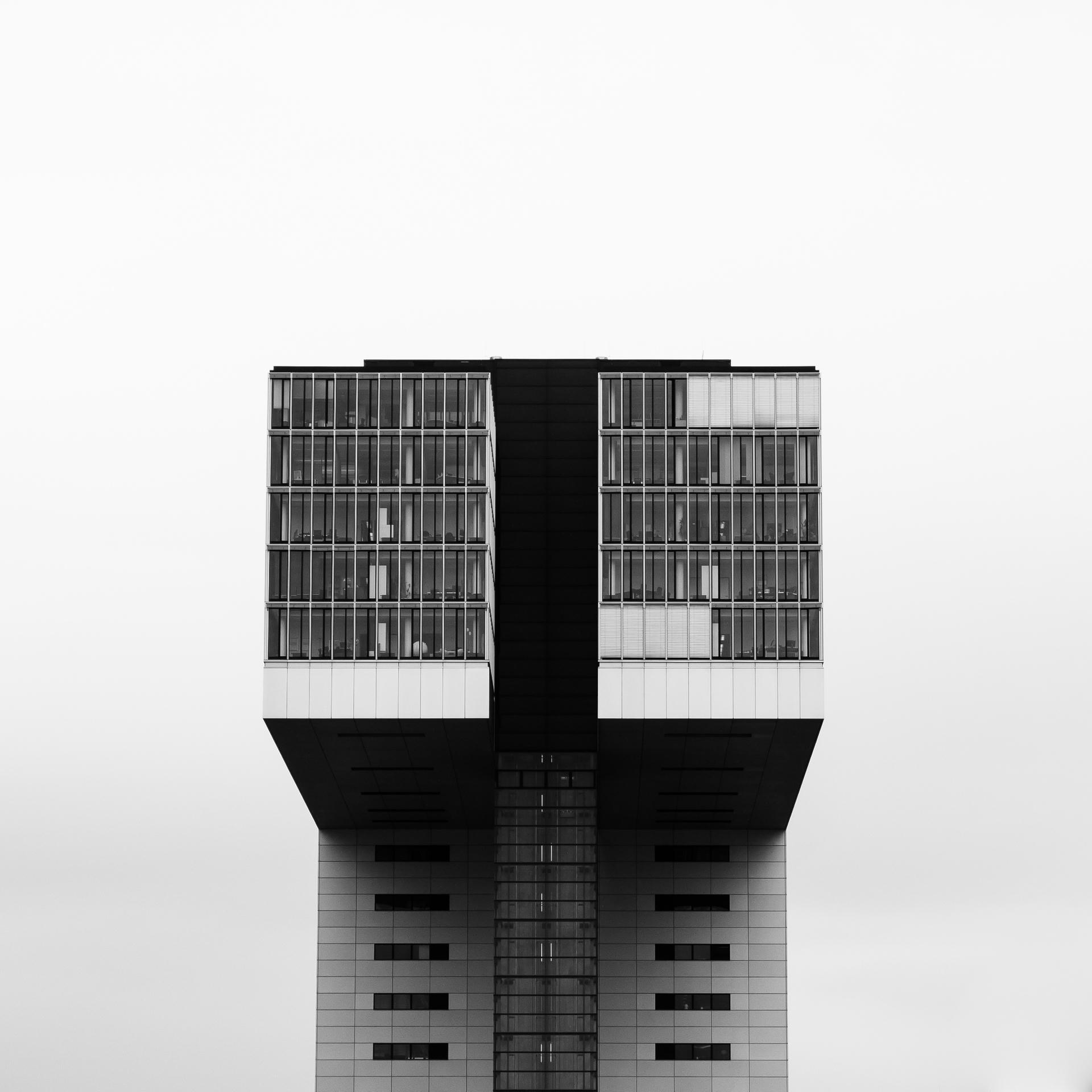 Tall building with two rectangular towers, connected by a horizontal section, against foggy sky.