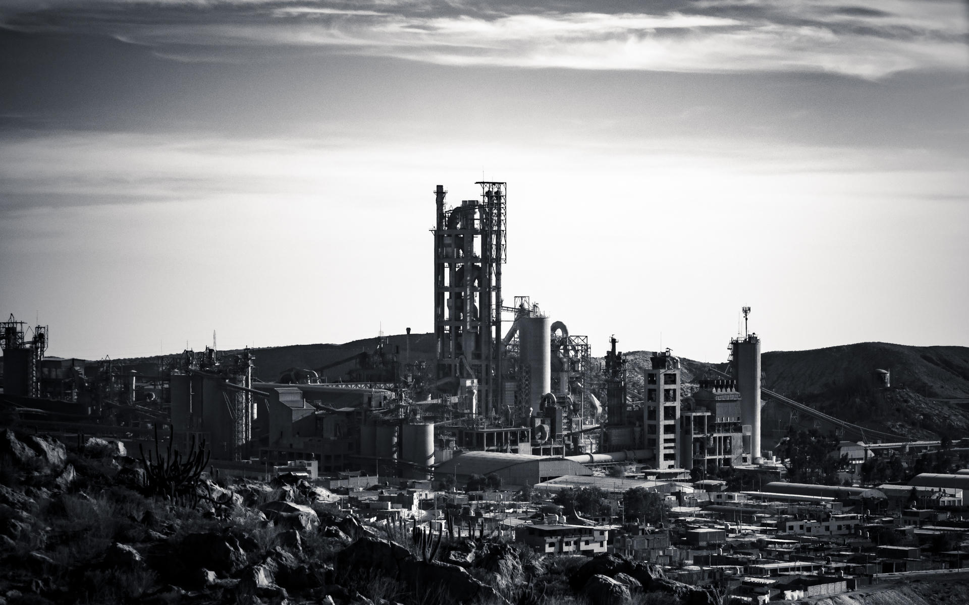 Industrial complex with towering structures, set against a hillside, captured in black and white.