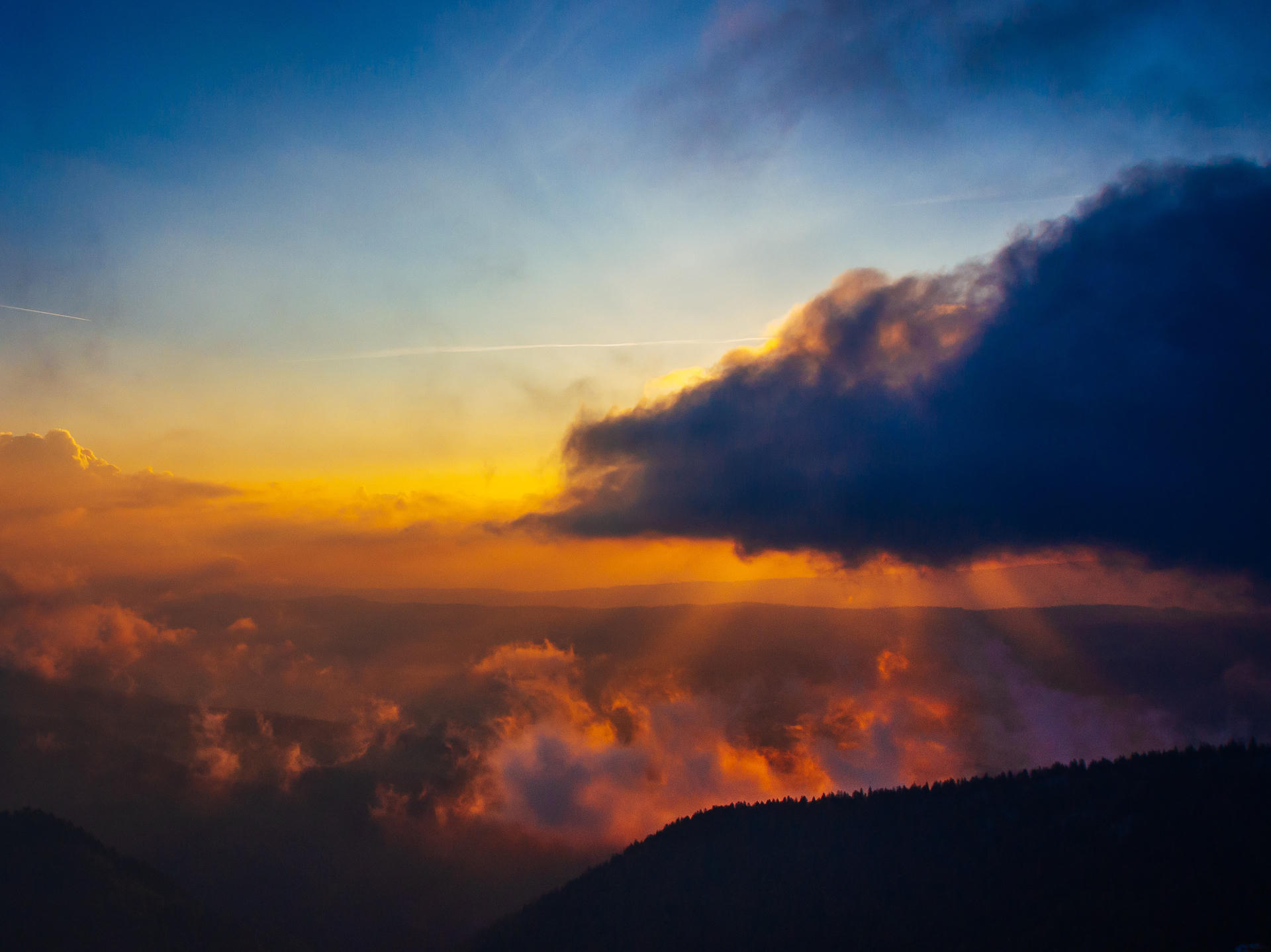 Sunset with vibrant orange and yellow clouds above dark silhouette of hills.