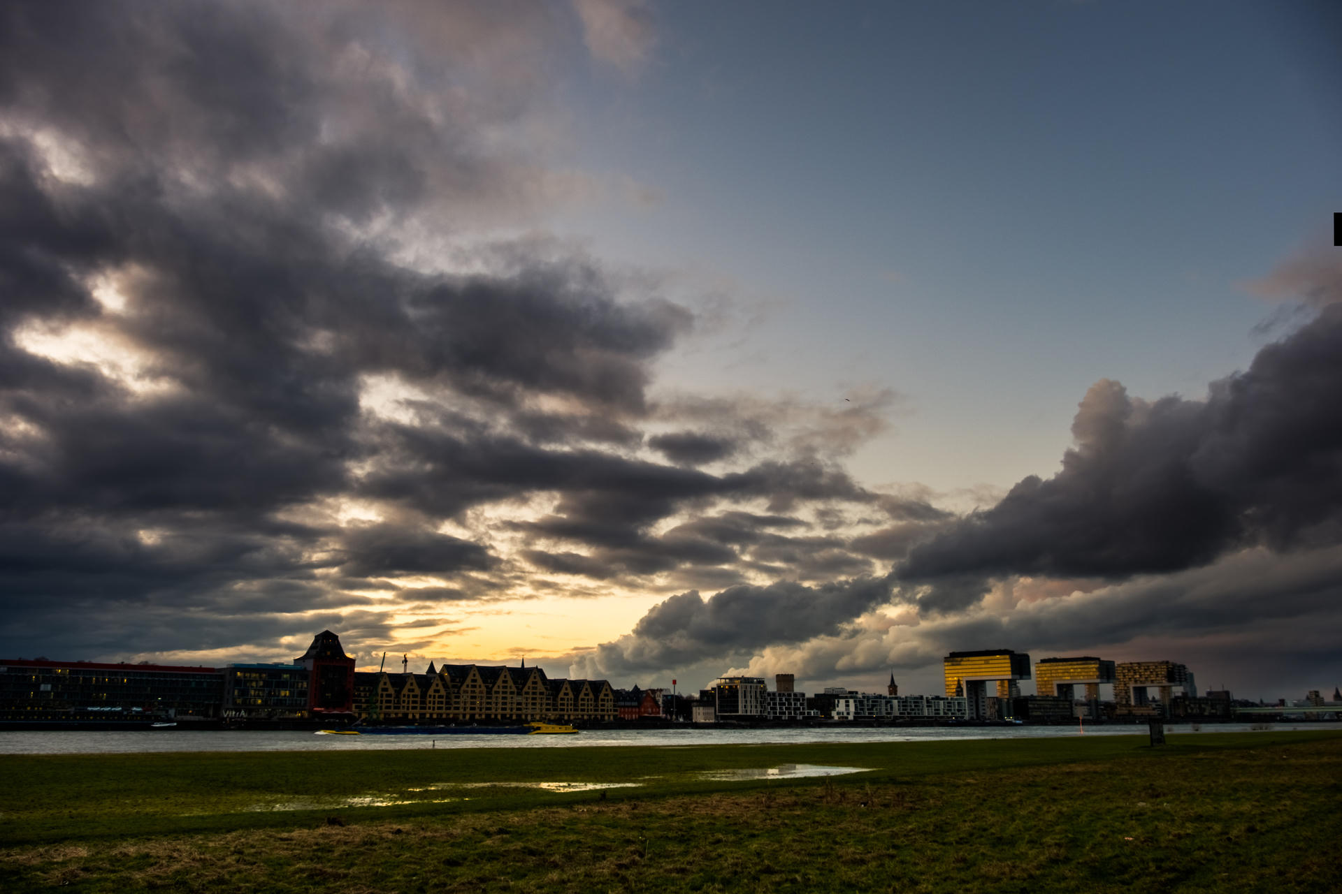 Dark clouds over city skyline at sunset, with green field in foreground.