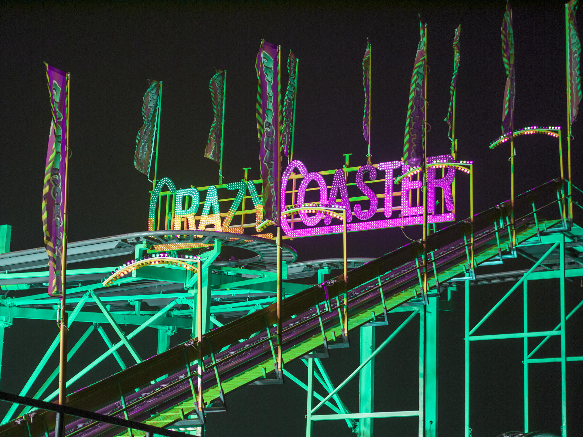 Neon signs on a roller coaster track at night.