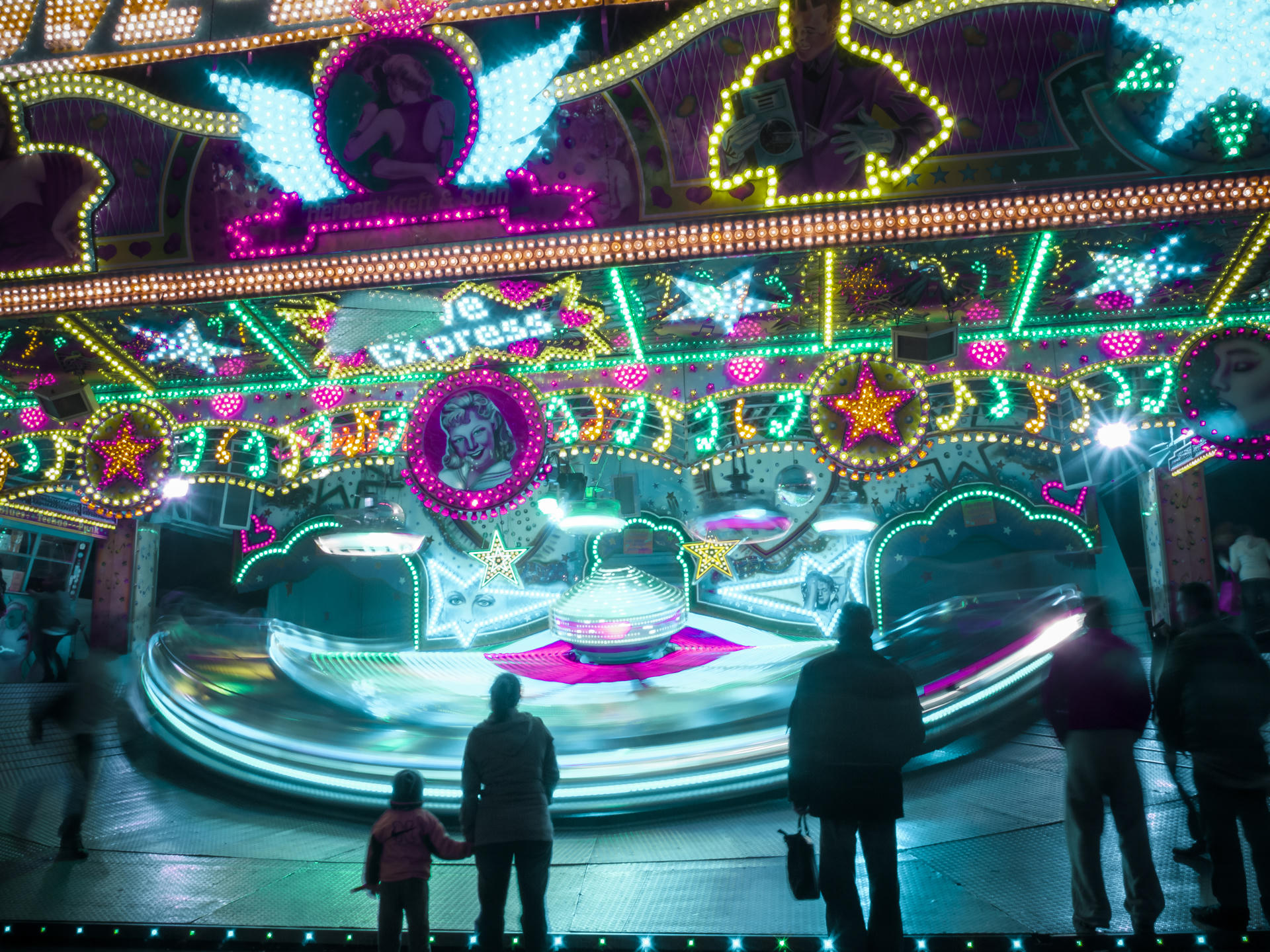 Colorful carousel at night with illuminated lights, a family watching, vibrant decorations.