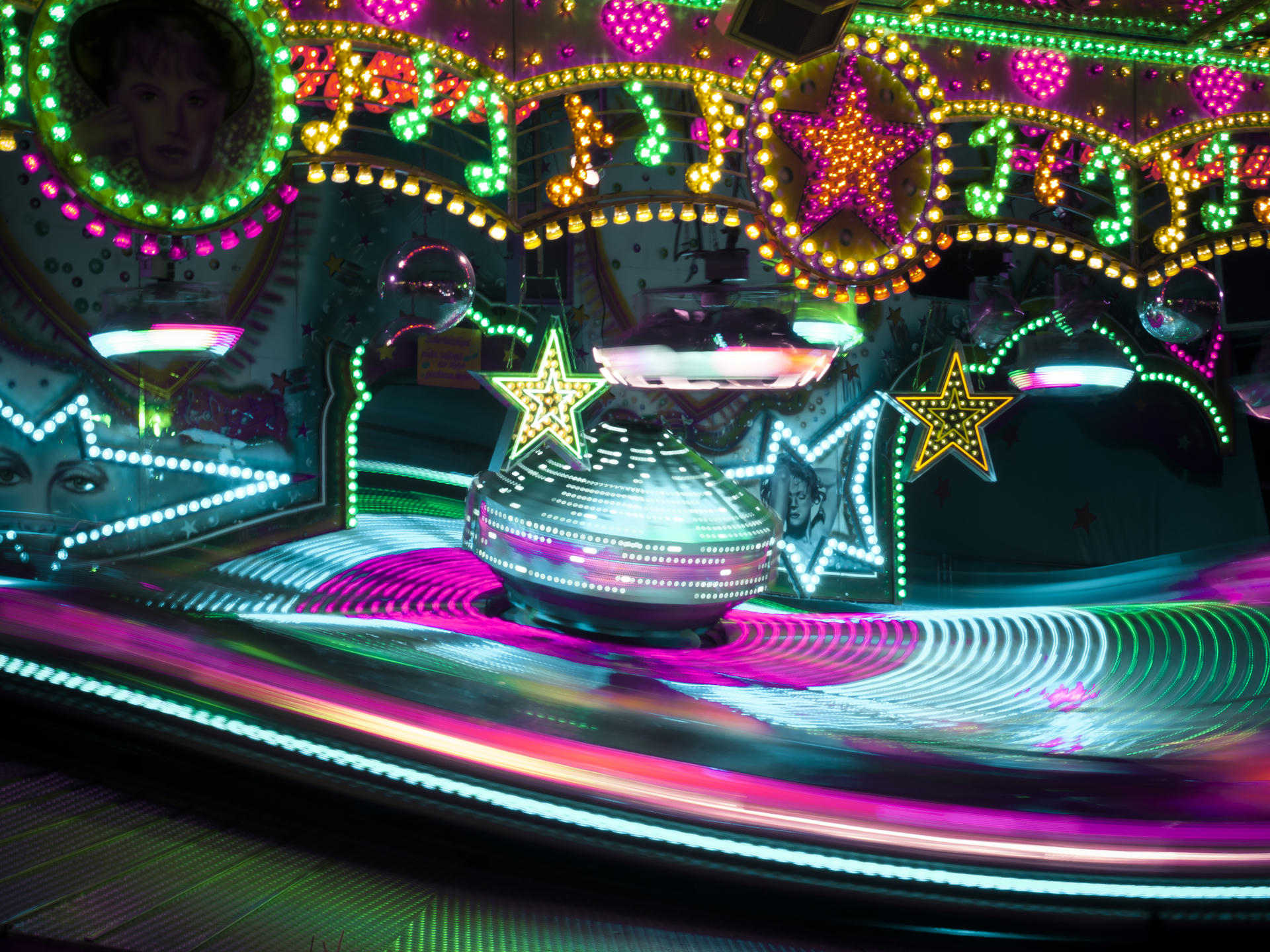 Colorful spinning carnival ride with bright neon lights, stars, and circular patterns at night.